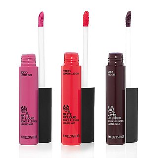 The image features three tubes of liquid lipsticks from The Body Shop. Each tube is designed with a sleek black cap and displays the shade names: 1. **Tokyo Lotus 024** - a vibrant pink. 2. **Sydney Amaryllis 004** - a bold red. 3. **Sicily Iris 019** - a deep, rich purple. Each tube includes a wand applicator for easy application, and they are labeled as "Matte Lip Liquid."